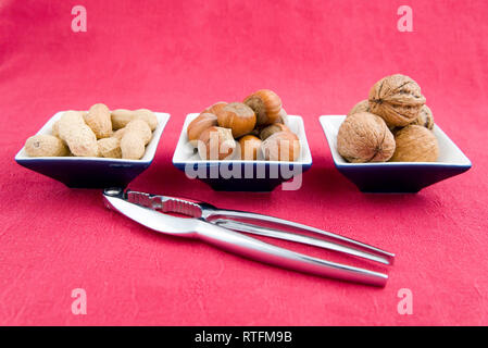walnuts, hazelnuts and peanuts in three bowls on red background Stock Photo