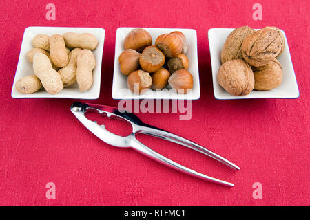 walnuts, hazelnuts and peanuts in three bowls on red background Stock Photo