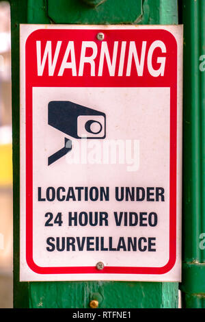 Warning sign on location under video surveillance. Close up view of a Warning sign on a green wooden post. A warning sign on a location that is under  Stock Photo