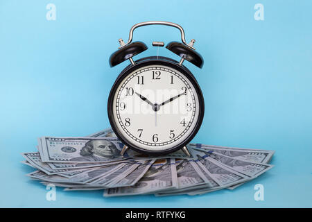 Black retro alarm clock and dollars on a blue colored background. Concept - time is money Stock Photo