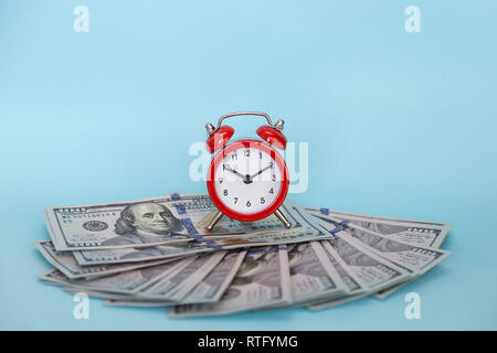 Red retro alarm clock and dollars on a blue background. Concept - time is money Stock Photo