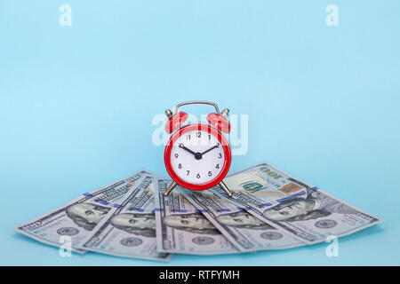 Red retro alarm clock and dollars on a colored background. Concept - time is money Stock Photo