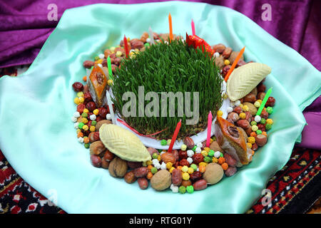 Novruz concept plate of traditional Azerbaijan pastries packlava and shekerbura in copper vintage tray with wheat grass semeni on white wooden table b Stock Photo