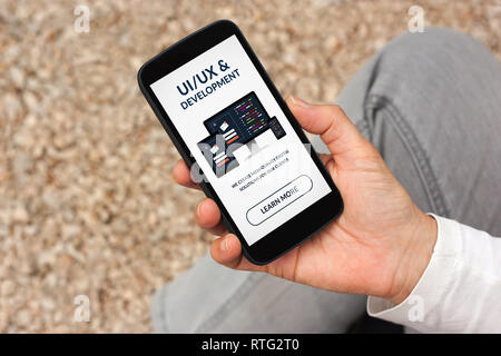 Hand holding smart phone with UI/UX design and development concept on screen. All screen content is designed by me Stock Photo