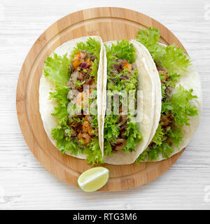 Shrimp tacos on round bamboo board on white wooden background, top view. Mexican cuisine. Flat lay, overhead, from above. Close-up. Stock Photo