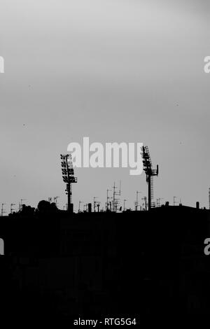 Silhouettes of two sport stadium lights at sunset, town of Matera, Basilicata region, Southern Italy. Black and white picture including some of the city buildings and roofs Stock Photo