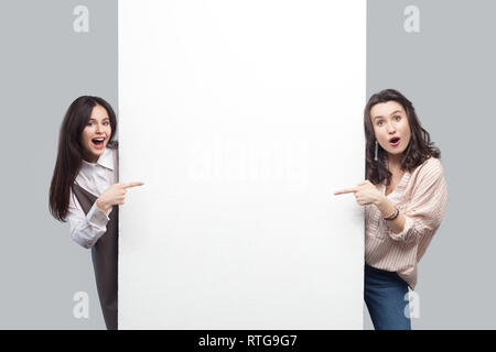 Portrait of surprised beautiful brunette young women in casual style standing, pointing at empty white blank copyspace and looking at camera with amaz Stock Photo