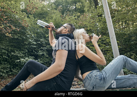 Alco addiction concept. Depressed and hopeless couple sitting after using drunk alcohol on the street Stock Photo