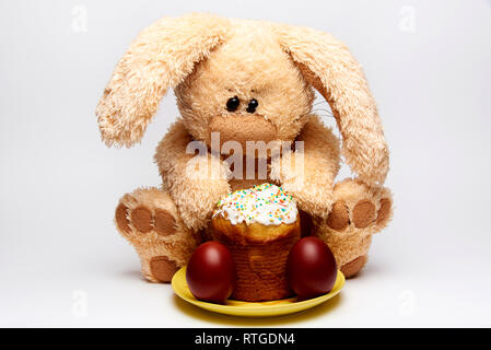 Stuffed soft rabbit with Easter cake and painted eggs on a white background. Stock Photo