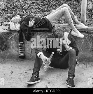 Alco addiction concept. Depressed and hopeless couple sitting after using drunk alcohol on the street Stock Photo