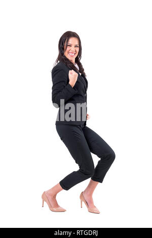 Ecstatic business woman in suit crouching with clenched fist celebrating success. Full body isolated on white background. Stock Photo