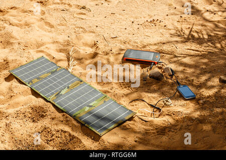 solar panel lying on the ground and charges the smart phone, the Sahara desert. Charge smart phone from the solar battery. Stock Photo