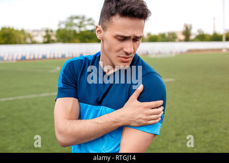 Young sportsman on stadium outside standing on lawn touching shoulder hurted close-up Stock Photo