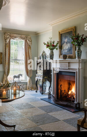 Lacquer cabinet at window with lit fire in hearth Stock Photo