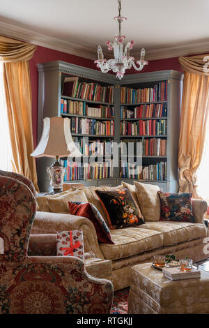 Corner bookcase with gold curtains and floral print sofa and chair Stock Photo