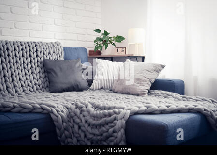 Gray knitted blanket from merino wool on couch with pillows in the interior of the living room Stock Photo