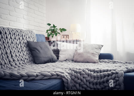 Gray knitted blanket from merino wool on couch with pillows in the interior of the living room Stock Photo