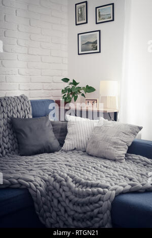 Gray knitted blanket from merino wool on couch with pillows in the interior of the living room. All photos in photo frames made by me. Stock Photo