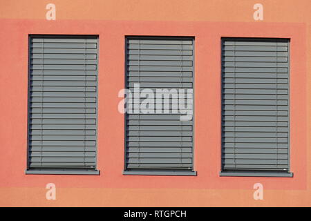 Window with dark shuttered blinds on a red house wall Stock Photo