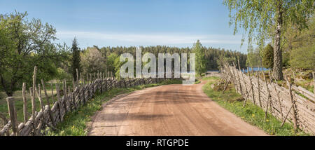 Picturesque country road leading to a lake through a beautiful rural landscape with roundpole fences, Smaland, Sweden, Scandinavia. Stock Photo