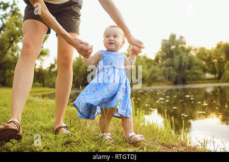 The baby with his mom takes the first steps in the park. Stock Photo