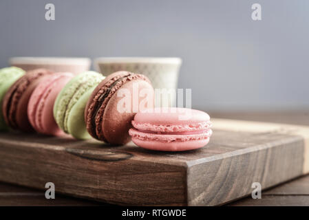 Different kinds of macaroons in row with tea cups on wooden background closeup Stock Photo