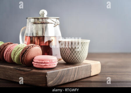 Different kinds of macaroons in row with teapot on wooden background closeup Stock Photo