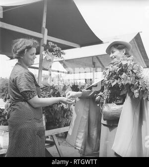 At the market in the 1940s. The young model and ballet dancer Gina Ohlsson at the flower market. She has just purchased a bouquet of syringa and pays the lady at the market stall. Photo Kristoffersson. Ref 134-1. Sweden June 1940 Stock Photo
