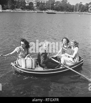 1940s summer. Four people are sitting in a very small rowing boat. They are all dressed nicely in summer dresses and picnic bags. The man rows it.  Photo Kristoffersson ref AC102-3. Sweden 1946 Stock Photo