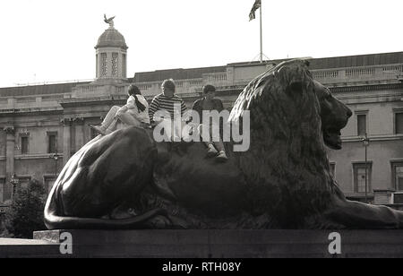 1970s, three teenage boys sitting on the back of one of the lion statues at Trafalgar Square, London, England, UK. The large bronze lions, designed by Sir Edwin Landseer and installed in 1867 to guard Nelson's Column, are a famous landmark in the city and a great place to climb up on and take in the view. Stock Photo