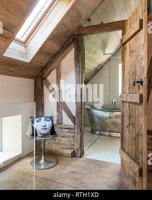 Fornasetti cushion at entrance to bathroom with door made from reclaimed Scandinavian pine scaffold boards Stock Photo