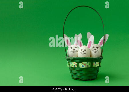 Busket with Easter bunny made from eggs and paper ears on green pastel background. Creative idea. Art food concept. Stock Photo
