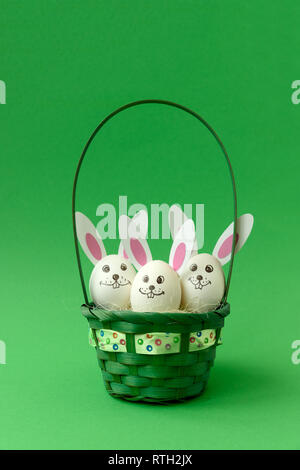 Busket with Easter bunny made from eggs and paper ears on green pastel background. Creative idea. Art food concept. Stock Photo