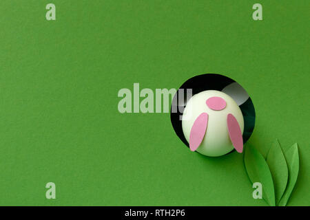 Easter bunny made from eggs and paper ears jump in hole on green pastel background. Creative idea. Art food concept. Stock Photo