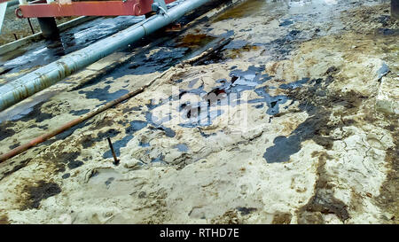 Spilled oil on sandy soil near pipelines and process equipment. Oil leaks during operation and repair Stock Photo