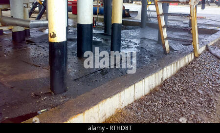 Spilled oil on sandy soil near pipelines and process equipment. Oil leaks during operation and repair Stock Photo