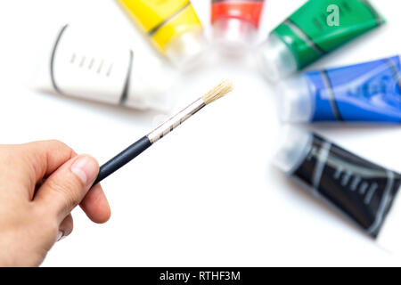 Man holding paint brush over colored paint tubes Stock Photo