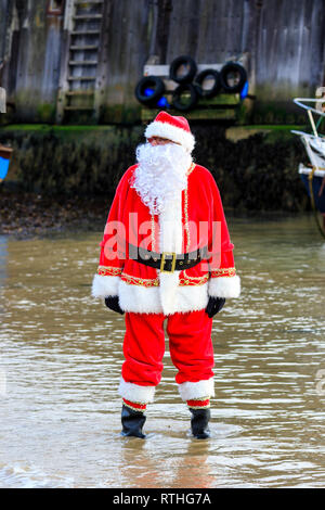 Man dressed as Father Christmas with long white fake beard, standing in the sea on the beach at Broadstairs during the annual New Year Day dip. Stock Photo
