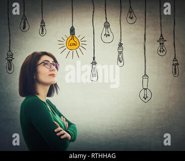 Businesswoman hands crossed wearing eyeglasses looking up thoughtfully as a lot of lightbulbs hanging and only one bulb is glowing while the others ar Stock Photo