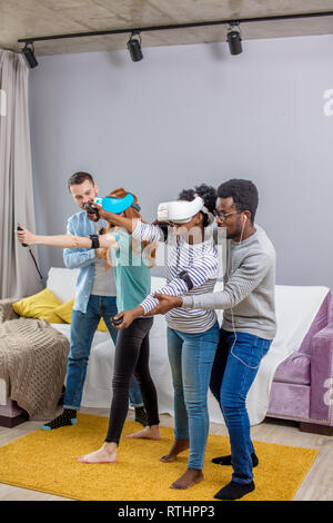 Virtual battle of two multiracial teams, consisting of loving african and caucasian couples playing in virtual reality game Guys support and teach the Stock Photo