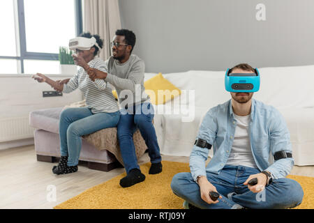 Multiracial students with focus on cauvasian man, are having fun using vr headset, sitting in campus room Stock Photo