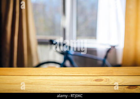 Product Placement Background. Wooden Table Against Blurry Interior of Cyclist's Living Room with Large Window and Blue Sport Bicycle Stock Photo