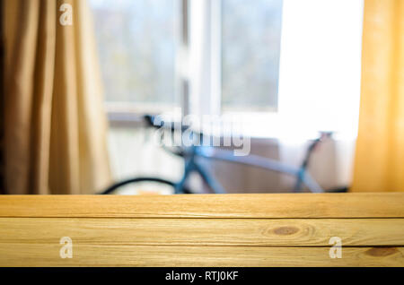 Product Placement Background. Wooden Table Against Blurry Interior of Cyclist's Living Room with Large Window and Blue Sport Bicycle Stock Photo