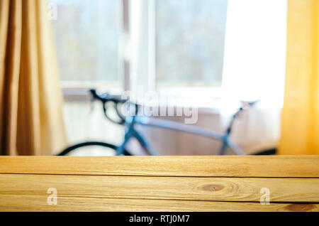 Product Placement Background. Wooden Table Against Blurry Interior of Cyclist's Living Room with Large Window and Blue Sport Bicycle Stock Photo
