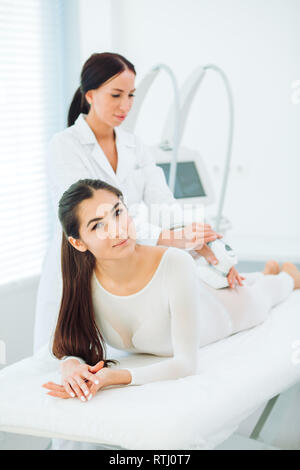 Lymphatic drainage massage LPG apparatus process. Pleased caucasian woman smiling at camera on a massage table getting a lpg massage on her body Stock Photo