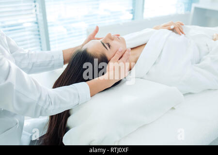 Facial spa cosmetology procedure, top view. Skin care lift anti age massage. Caucasian brunette woman dressed in white bathrobe, receiving anti-wrinkl