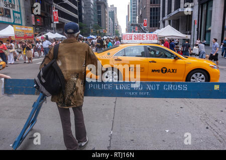 Man in a Police Line Do Not Crossing barrier in 6th Avenue closing to car only for pedestrian with food stands in Manhattan, New York, USA Stock Photo