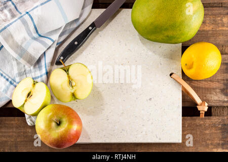 Concrete stone server with space for text on rustic wood plank surface. Arranged apples, lemon and mango, knife and cloth. Top view, flat lay. Stock Photo
