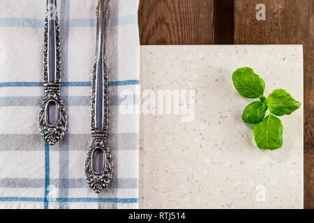 Concrete stone server with space for text on rustic wood plank surface. Arranged cutlery, cloth and basil. Top view, flat lay, from above, overhead. Stock Photo