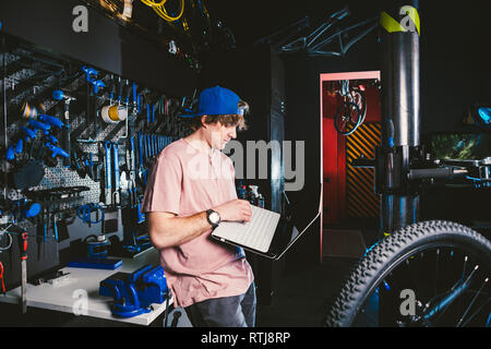 Theme business profession manager and technology. Young stylish Caucasian male owner bicycle shop uses a laptop computer near the stand with the tools Stock Photo